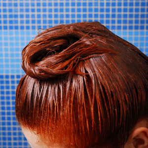Red hair dye applied to long hair against a blue background.